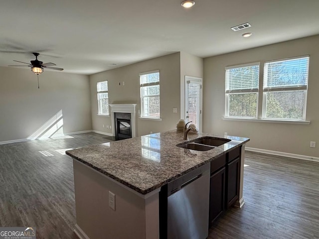 kitchen with stainless steel dishwasher, ceiling fan, a kitchen island with sink, sink, and stone counters