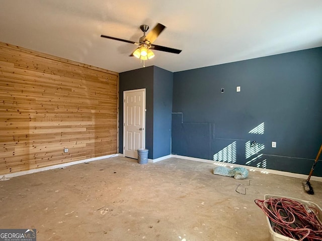 empty room featuring wood walls, ceiling fan, and concrete flooring