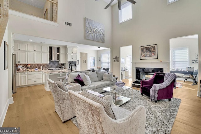 living room featuring a towering ceiling, light hardwood / wood-style flooring, plenty of natural light, and ceiling fan