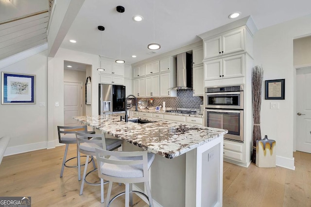 kitchen featuring white cabinets, sink, wall chimney exhaust hood, appliances with stainless steel finishes, and decorative light fixtures