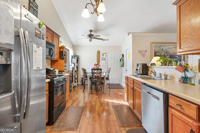 kitchen with sink, decorative light fixtures, vaulted ceiling, light hardwood / wood-style flooring, and black appliances