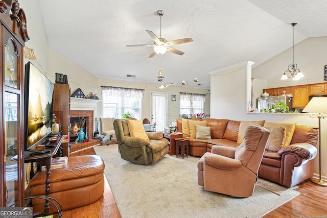 living room featuring a brick fireplace, light hardwood / wood-style flooring, a textured ceiling, and vaulted ceiling