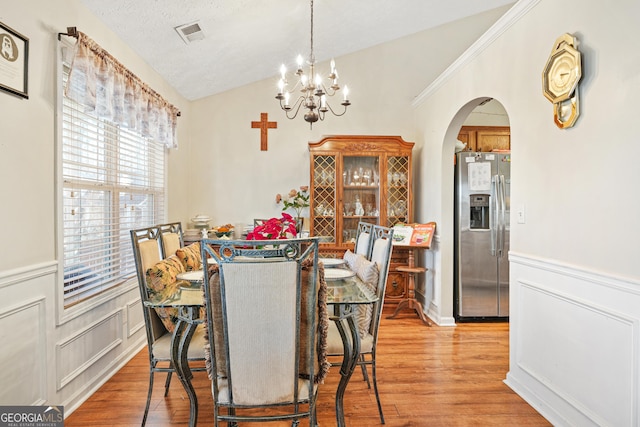 dining room with lofted ceiling, light hardwood / wood-style floors, a textured ceiling, and an inviting chandelier