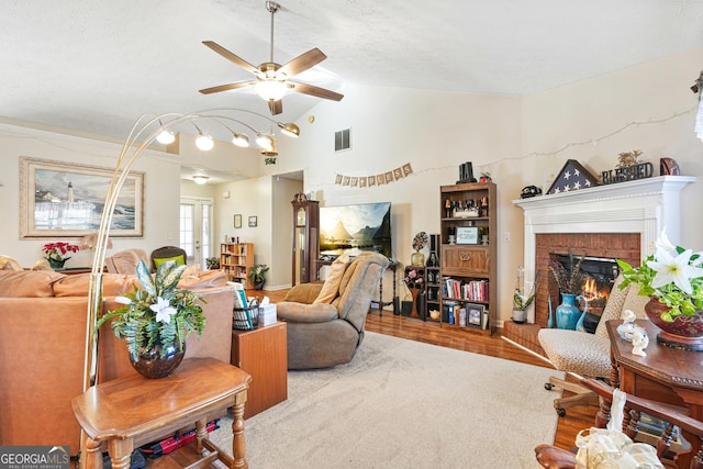 living room with vaulted ceiling, carpet flooring, ceiling fan, a brick fireplace, and a textured ceiling