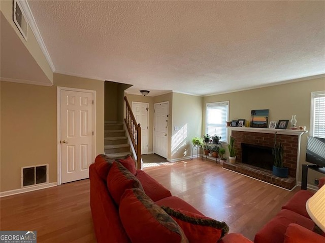 living room featuring a fireplace, wood-type flooring, a textured ceiling, and ornamental molding