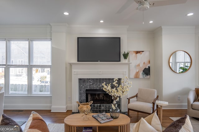 living room featuring dark wood-type flooring, ceiling fan, a premium fireplace, and crown molding