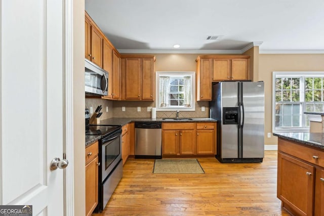 kitchen with decorative backsplash, appliances with stainless steel finishes, dark stone counters, ornamental molding, and sink