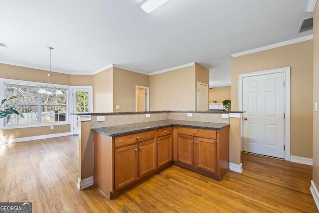 kitchen with hanging light fixtures, dark stone countertops, light wood-type flooring, a kitchen island, and a chandelier