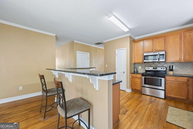 kitchen featuring a breakfast bar, decorative backsplash, light wood-type flooring, ornamental molding, and stainless steel appliances