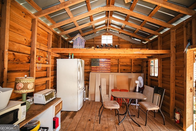 interior space with lofted ceiling, wooden walls, white appliances, and hardwood / wood-style floors