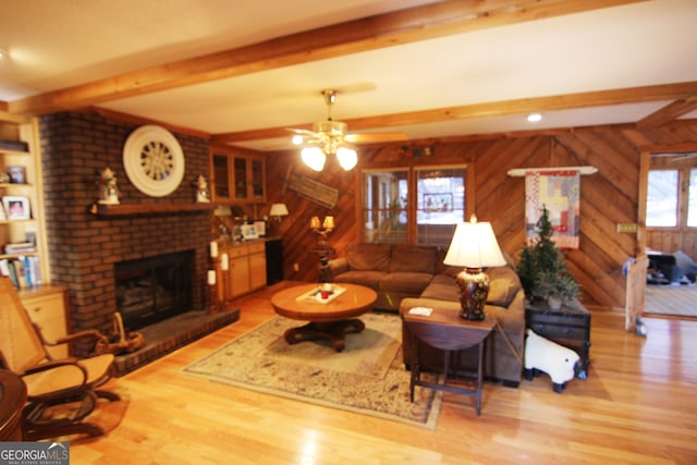 living room with light wood-type flooring, a brick fireplace, ceiling fan, wooden walls, and beamed ceiling