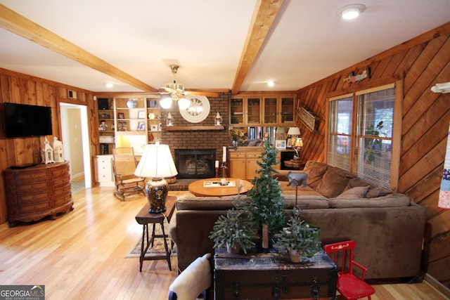 living room featuring beam ceiling, built in features, wooden walls, and a brick fireplace