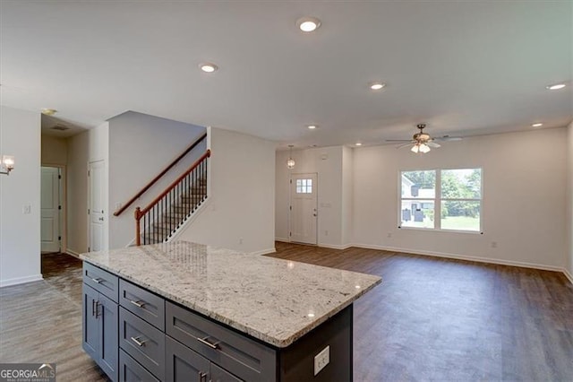 kitchen with ceiling fan with notable chandelier, a kitchen island, light stone counters, and dark wood-type flooring