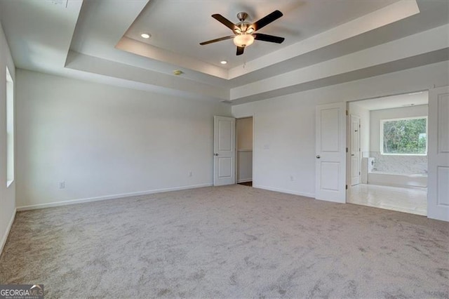 unfurnished bedroom featuring ceiling fan, connected bathroom, a raised ceiling, and carpet floors