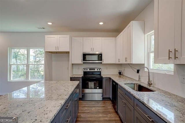 kitchen with light stone counters, dark wood-type flooring, white cabinets, appliances with stainless steel finishes, and sink