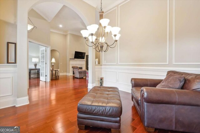 living area with crown molding, wood-type flooring, and an inviting chandelier