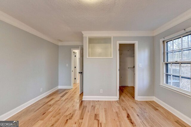 unfurnished bedroom featuring a walk in closet, crown molding, a textured ceiling, light hardwood / wood-style floors, and a closet