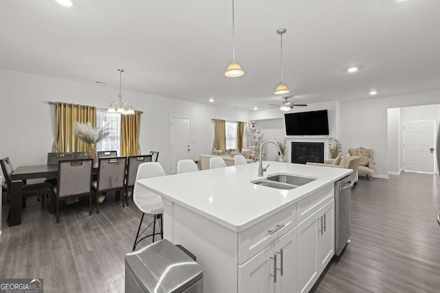 kitchen featuring ceiling fan with notable chandelier, sink, pendant lighting, a center island with sink, and white cabinetry