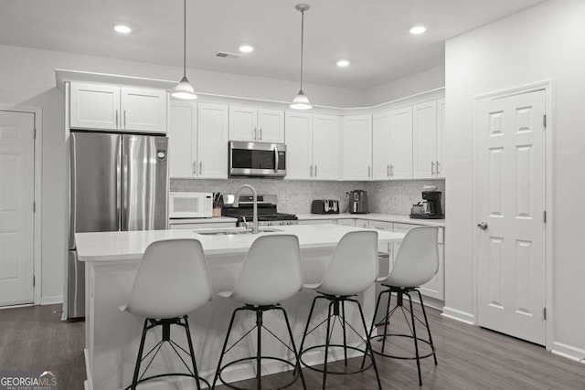 kitchen with appliances with stainless steel finishes, white cabinetry, hanging light fixtures, and a kitchen island with sink