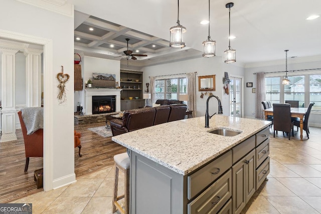 kitchen with light stone countertops, sink, hanging light fixtures, ceiling fan, and coffered ceiling