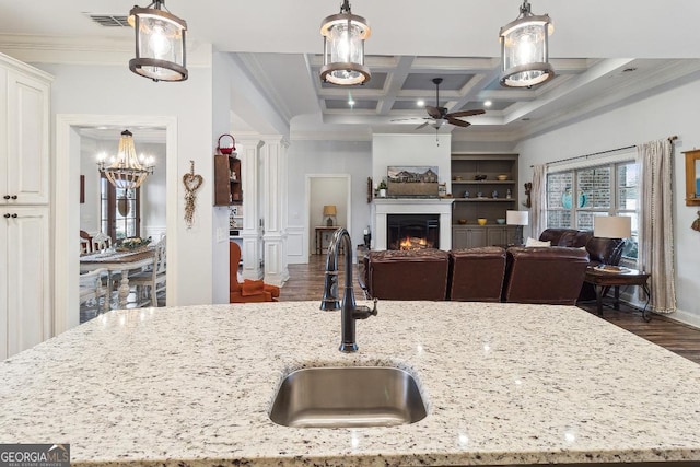 kitchen with light stone counters, sink, hanging light fixtures, and coffered ceiling