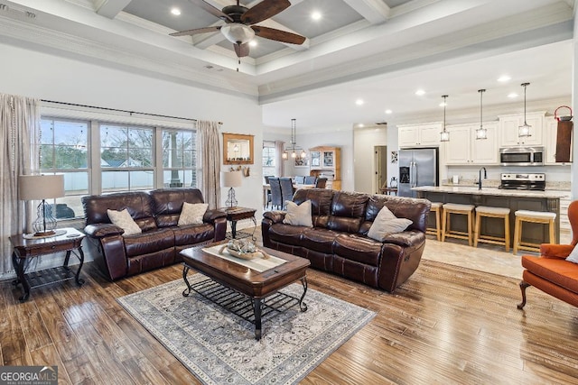 living room featuring beam ceiling, sink, crown molding, hardwood / wood-style flooring, and ceiling fan with notable chandelier