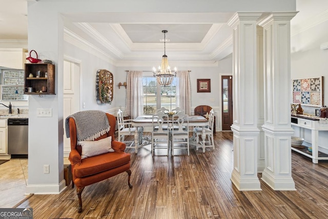 dining area featuring wood-type flooring, a tray ceiling, an inviting chandelier, ornamental molding, and decorative columns