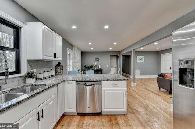 kitchen with kitchen peninsula, appliances with stainless steel finishes, light stone counters, light hardwood / wood-style flooring, and white cabinetry