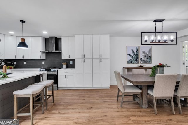 kitchen featuring white cabinets, gas stove, hanging light fixtures, and wall chimney exhaust hood