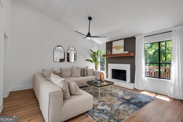 living room with ceiling fan, a large fireplace, light wood-type flooring, and vaulted ceiling