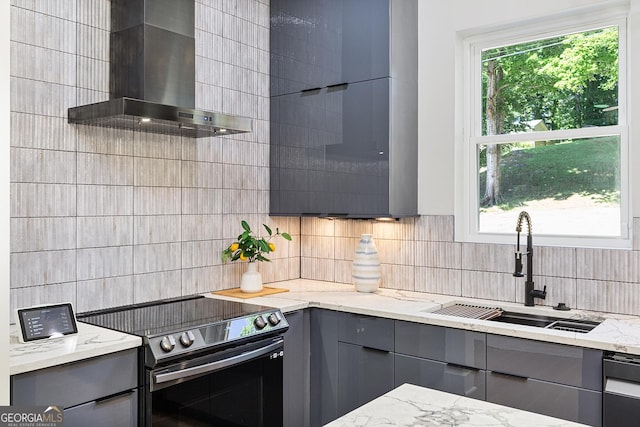 kitchen with sink, light stone counters, wall chimney exhaust hood, gray cabinets, and range with electric stovetop