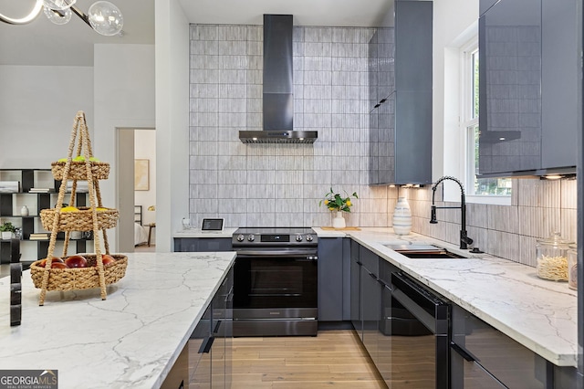 kitchen with light stone counters, wall chimney exhaust hood, sink, stainless steel range with electric cooktop, and backsplash