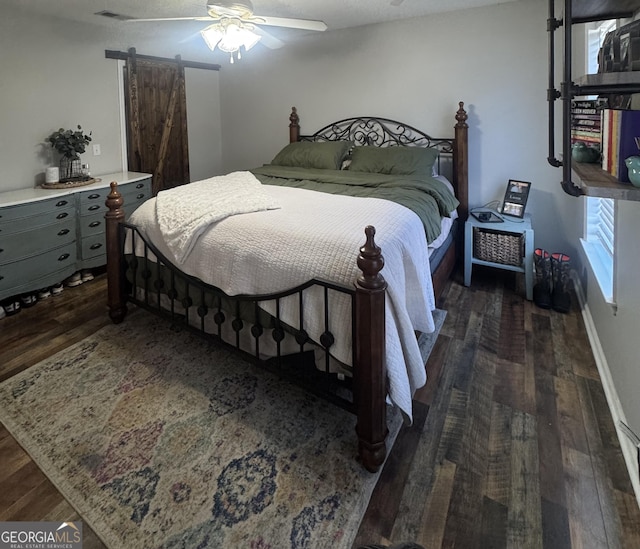 bedroom featuring a barn door, dark hardwood / wood-style floors, and ceiling fan