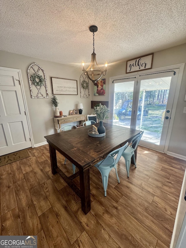 dining area with wood-type flooring, a textured ceiling, and an inviting chandelier