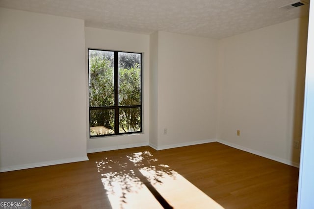 empty room with plenty of natural light, a textured ceiling, and hardwood / wood-style flooring