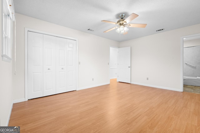 unfurnished bedroom featuring light hardwood / wood-style flooring, ensuite bath, ceiling fan, a textured ceiling, and a closet