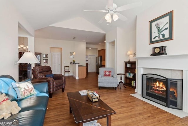 living room featuring ceiling fan with notable chandelier, wood-type flooring, lofted ceiling, and a fireplace