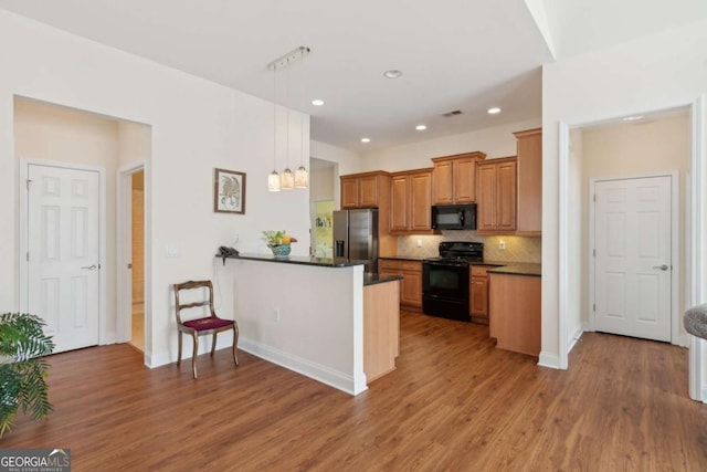 kitchen with hanging light fixtures, tasteful backsplash, kitchen peninsula, wood-type flooring, and black appliances