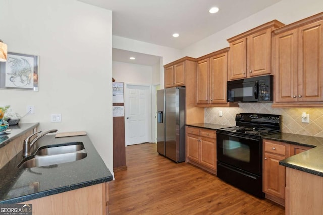 kitchen with sink, tasteful backsplash, dark stone countertops, black appliances, and light wood-type flooring