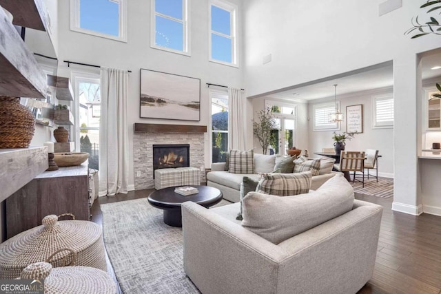 living room featuring a towering ceiling, dark hardwood / wood-style floors, a wealth of natural light, and a stone fireplace