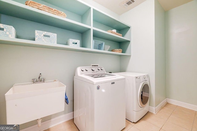 clothes washing area with light tile patterned floors, separate washer and dryer, and sink