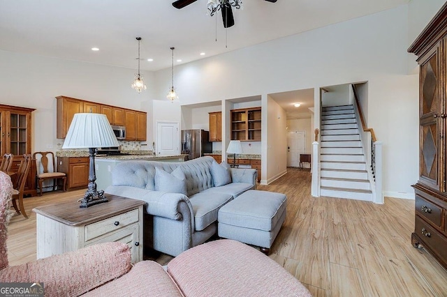 living room with ceiling fan, light hardwood / wood-style flooring, and a towering ceiling