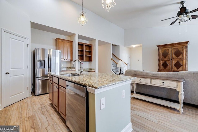 kitchen featuring light stone countertops, stainless steel appliances, a kitchen island with sink, sink, and pendant lighting