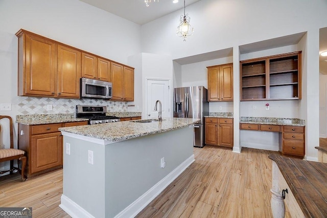 kitchen featuring a towering ceiling, stainless steel appliances, sink, hanging light fixtures, and an island with sink