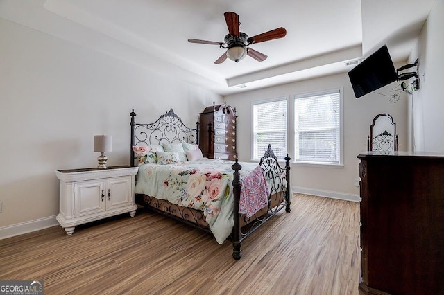 bedroom featuring a tray ceiling, ceiling fan, and light hardwood / wood-style flooring