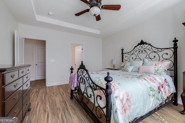 bedroom with light hardwood / wood-style floors, a raised ceiling, and ceiling fan