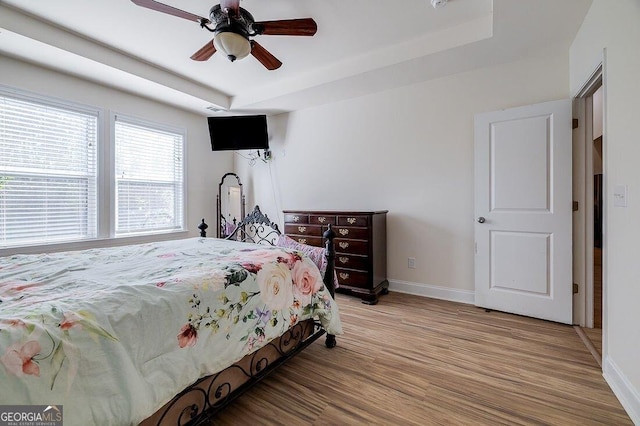 bedroom featuring ceiling fan, a raised ceiling, and light wood-type flooring