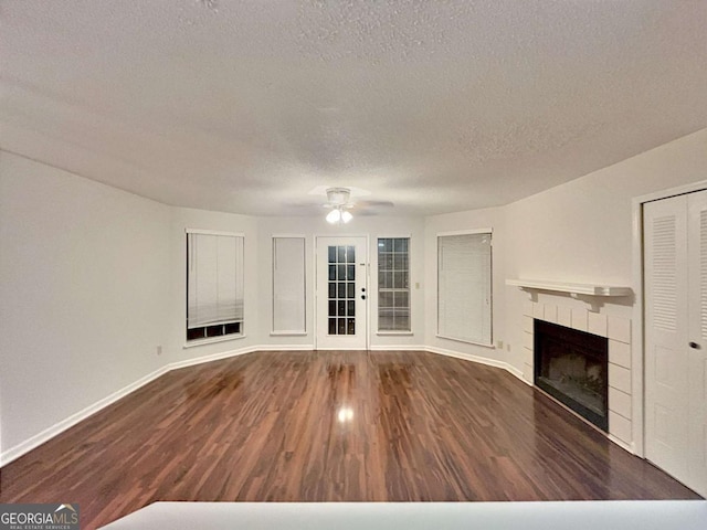 unfurnished living room featuring ceiling fan, dark hardwood / wood-style floors, a tile fireplace, and a textured ceiling