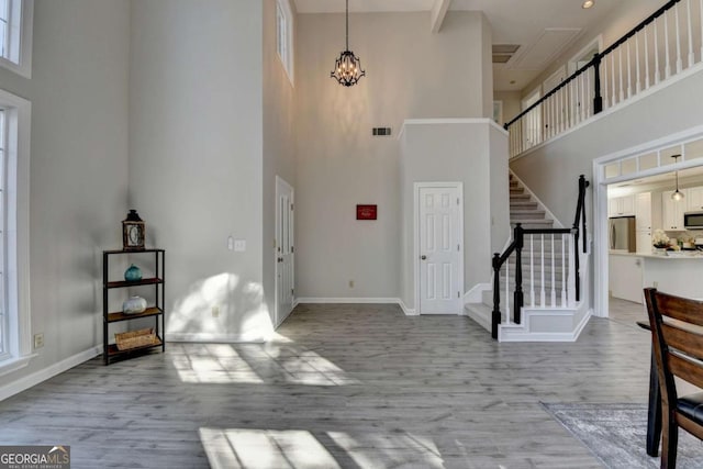 entrance foyer featuring a towering ceiling, an inviting chandelier, light hardwood / wood-style flooring, and plenty of natural light