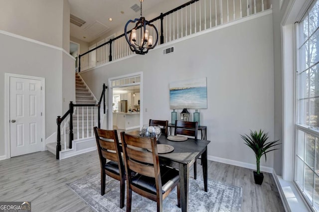 dining area with a towering ceiling, an inviting chandelier, and light hardwood / wood-style flooring